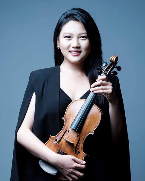 A women wearing smart black dress, holding a violin, smiling.